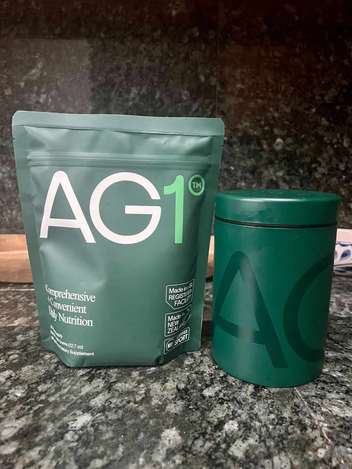 A styled shot of the complete AG1 starter kit, featuring the supplement pouch and the signature metal storage canister, sitting on a clean, modern marble countertop.