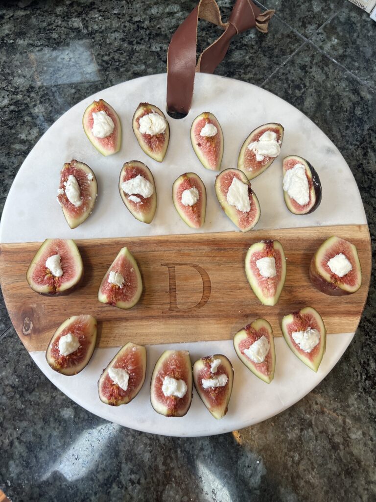 A white marble serving platter topped with fresh mission figs stuffed with creamy goat cheese, garnished with toasted walnuts and a balsamic glaze drizzle—a quick 10-minute appetizer for a dinner party.