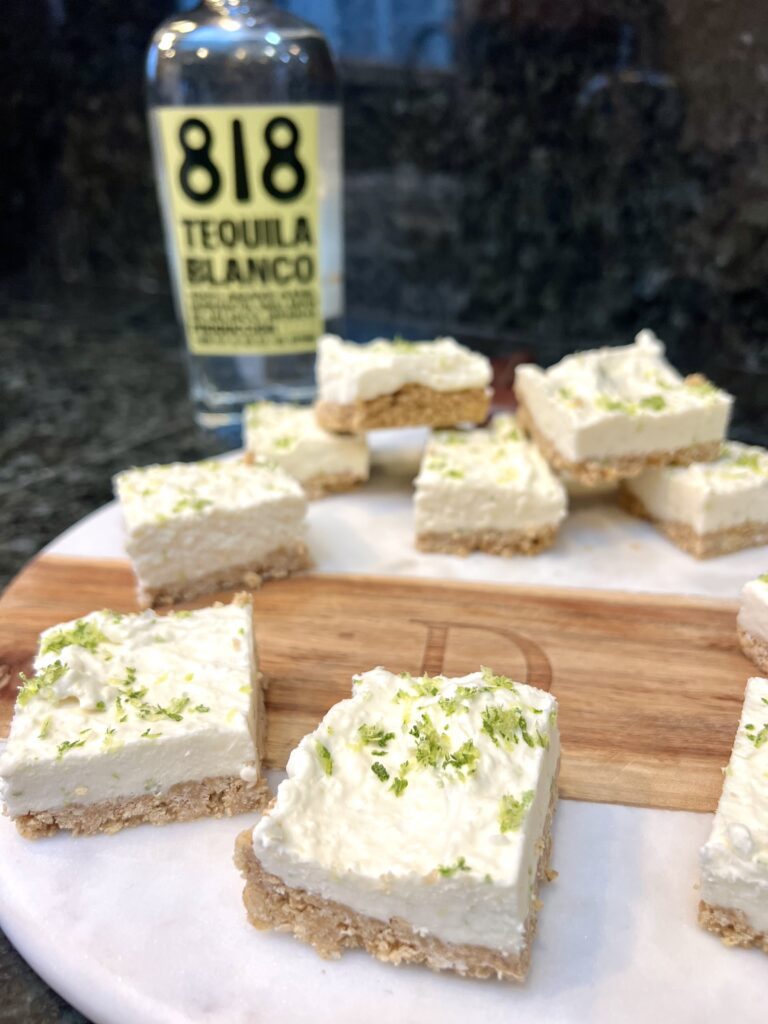 A platter of sliced no-bake margarita cheesecake bars topped with fresh lime zest and sea salt.