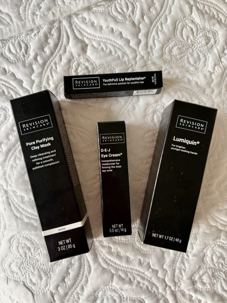 An authentic Revision Skincare review haul featuring four medical-grade products in their packaging, demonstrating a long-term user's skincare investment on a white bedspread.
