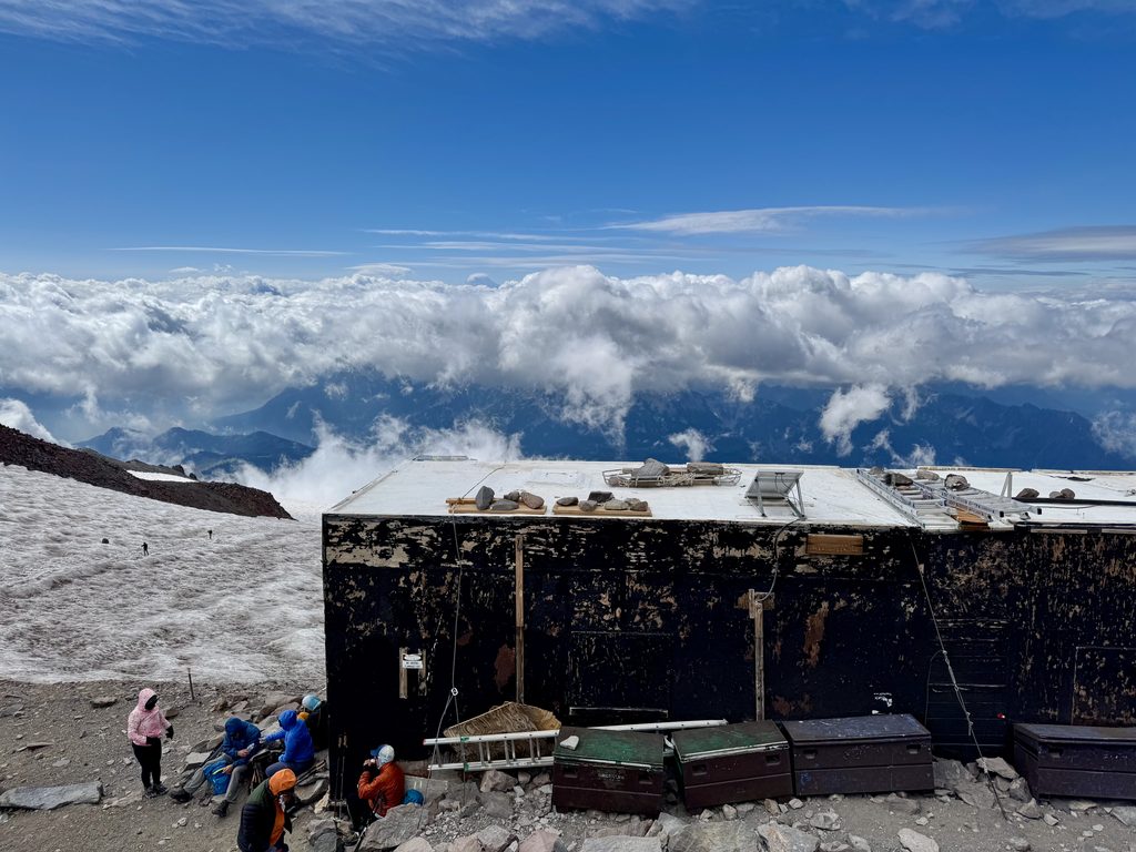 Historic stone shelter huts and high-alpine glacier views at Camp Muir on Mount Rainier at 10,188 feet.